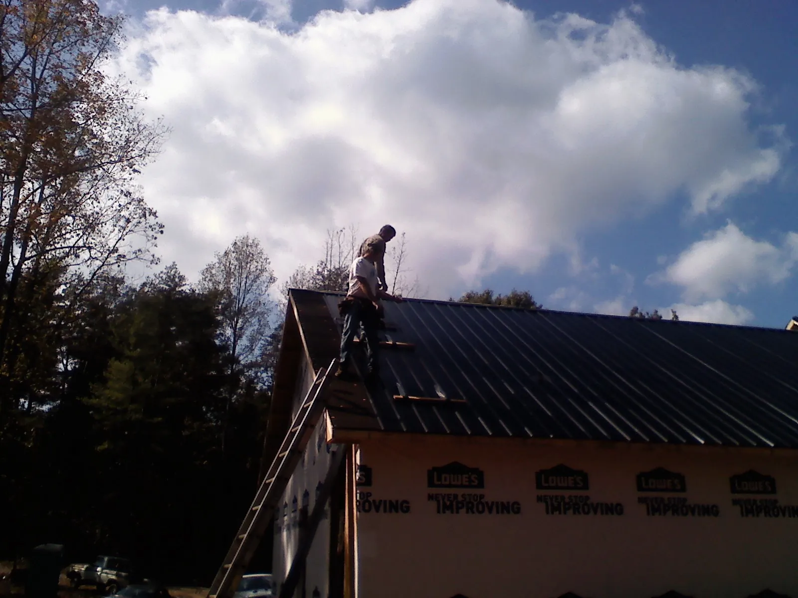 Roofer fastening dark metal panels high against a cloudy sky, from a Roof Inspection job in Waldo