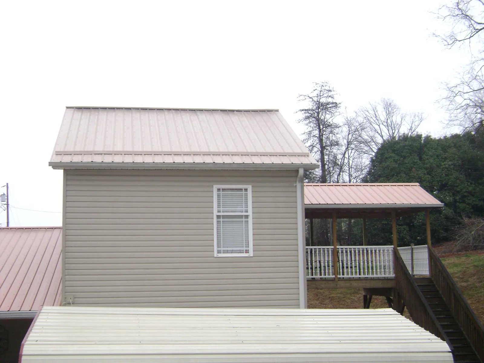 Tan metal roofs on a two story addition and attached porch, from a Roof Replacement job in Waldo